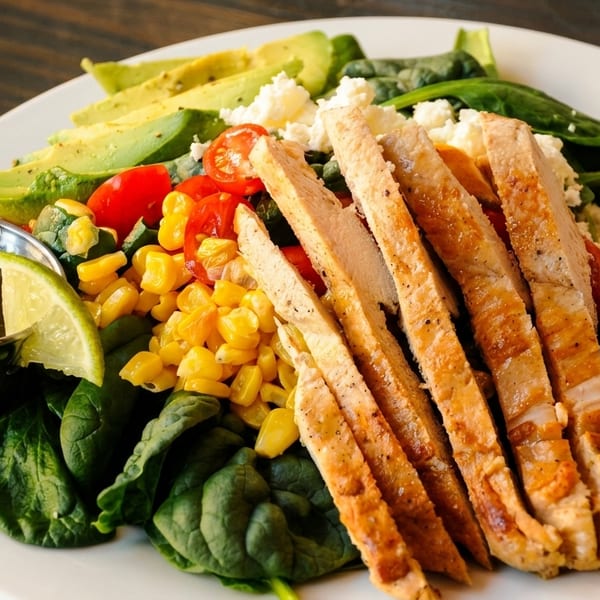 Grilled chicken salad with spinach, avocado, corn, tomatoes, feta, and a side of dressing.