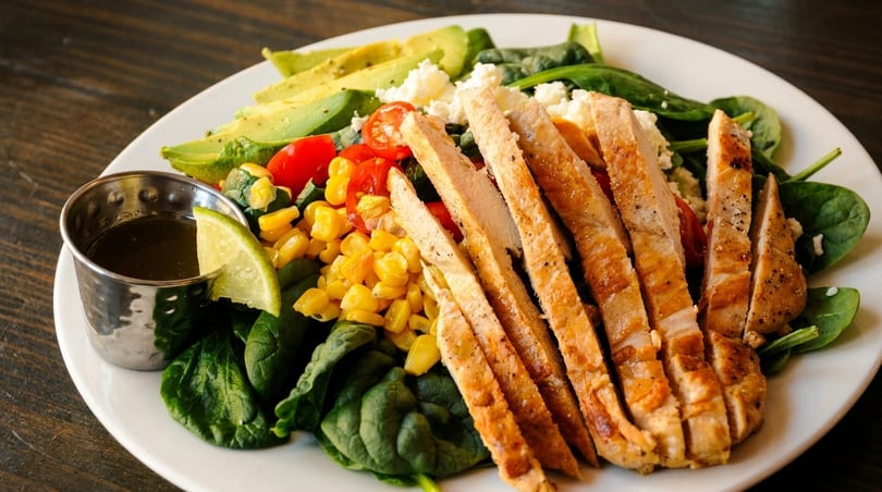 Grilled chicken salad with spinach, avocado, corn, tomatoes, feta, and a side of dressing.