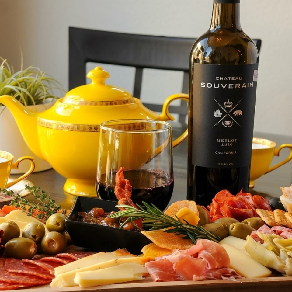 A charcuterie board with meats, cheeses, olives, and bread, next to a bottle of red wine.