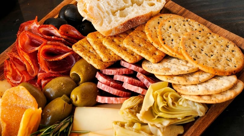 A wooden board filled with various meats, cheeses, olives, crackers, and bread.