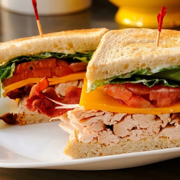 Two halves of a turkey club sandwich with bacon, cheese, lettuce, and tomato on toasted bread.