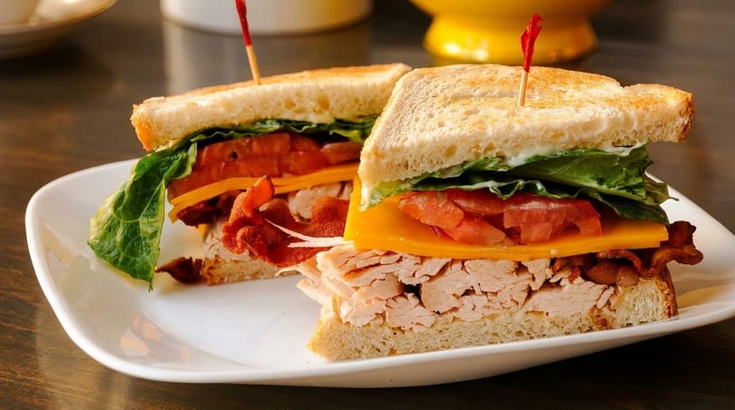 Two halves of a turkey club sandwich with bacon, cheese, lettuce, and tomato on toasted bread.
