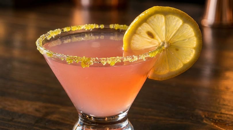 Pink cocktail in a martini glass with a sugar-rimmed edge and a lemon slice garnish.